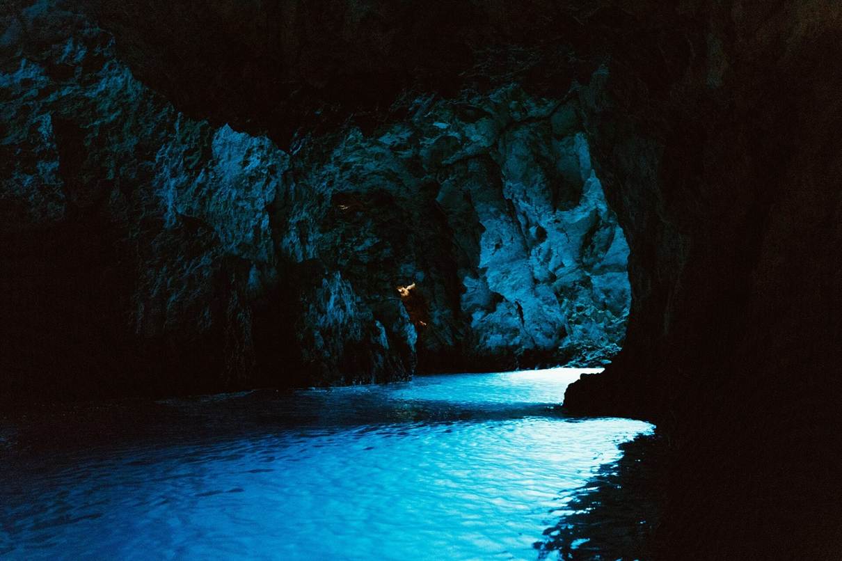 The image depicts a serene cave entrance with a small light shining from within, reflecting off the walls and creating a beautiful blue hue in the water.

Sadržaj generiran uz AI možda nije točan.